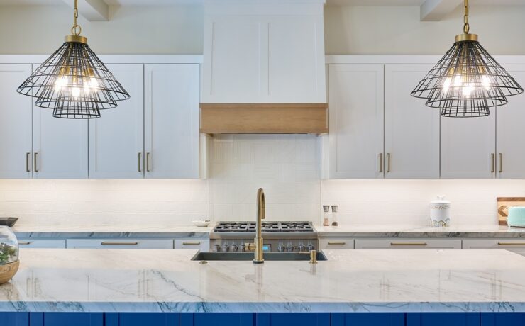 A kitchen with white and blue cabinets and a large island in the middle. Two overhead lights dangle above the counter.