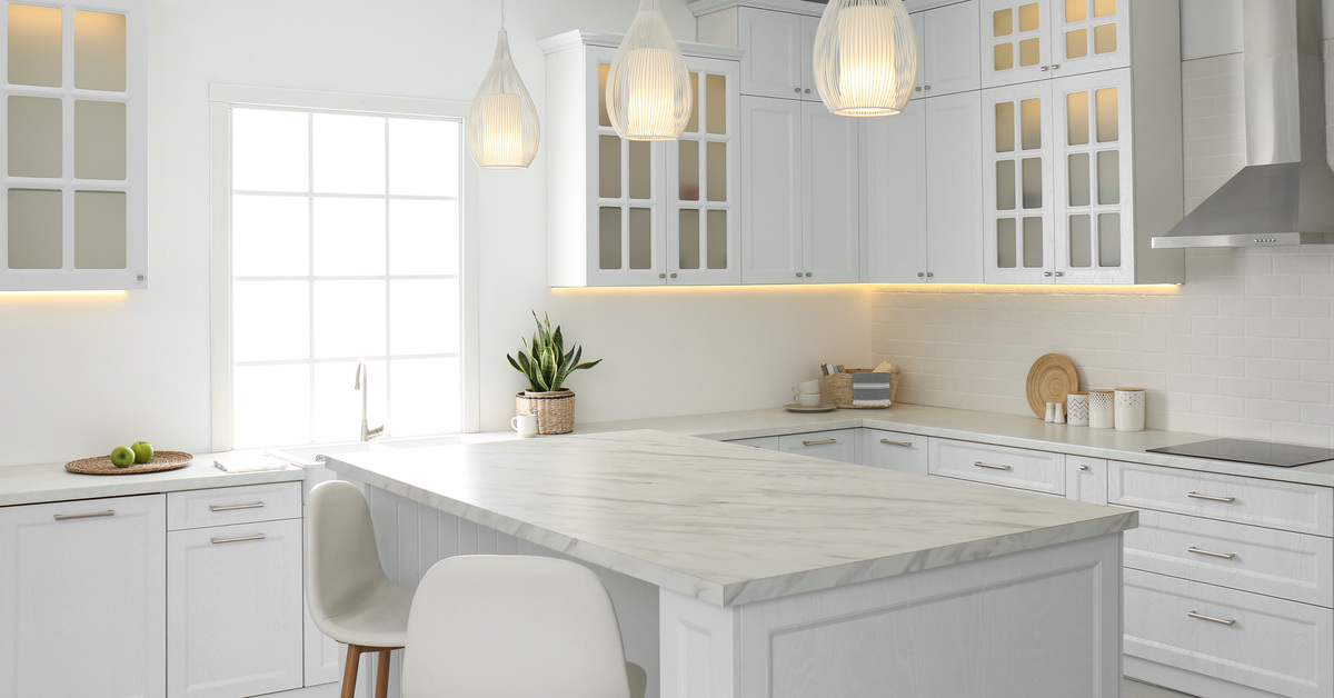 A beautiful, open kitchen that is very clean. The cabinets, counters, lights, and chairs are all white.