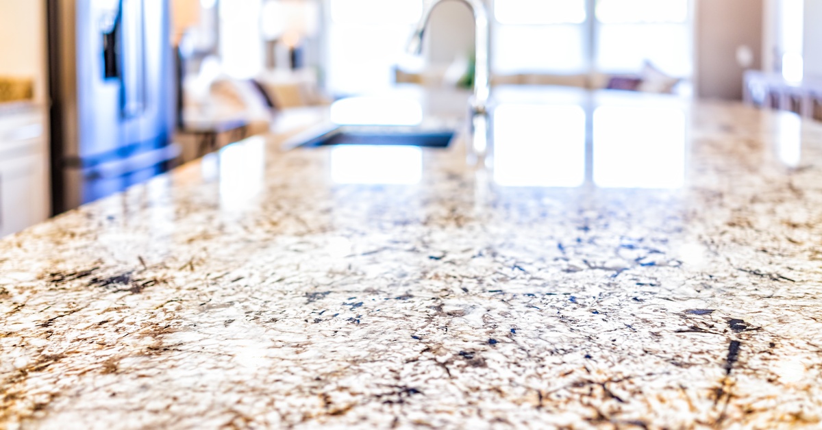 A close-up of a granite kitchen countertop. Bright sunlight reflects off the surface from nearby windows.
