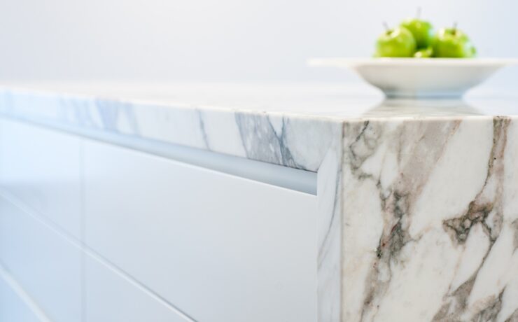 A side-view of the edge of a white and gray marble countertop. There is a bowl of green apples sitting on the counter.