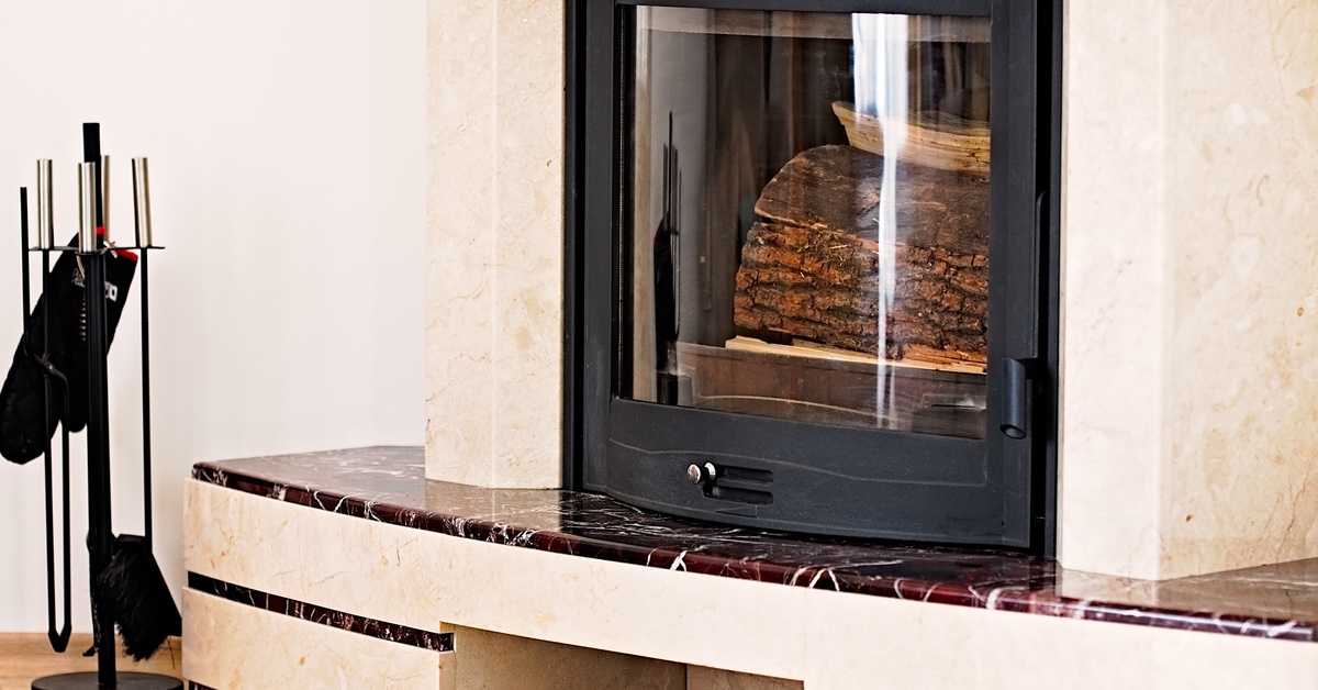 A fireplace with wood inside and tools next to it. The surround is a dark brown, marbled stone with round edges.