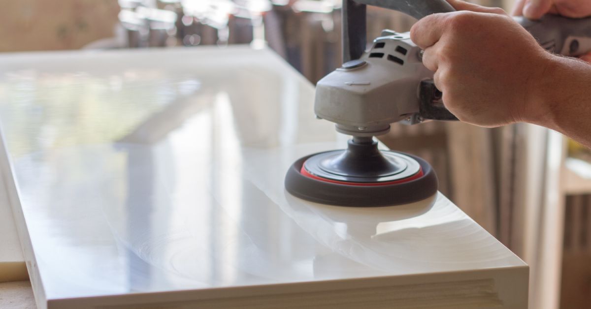 Someone holds a polishing machine against the surface of a cutout piece of stone. The surface is shiny.