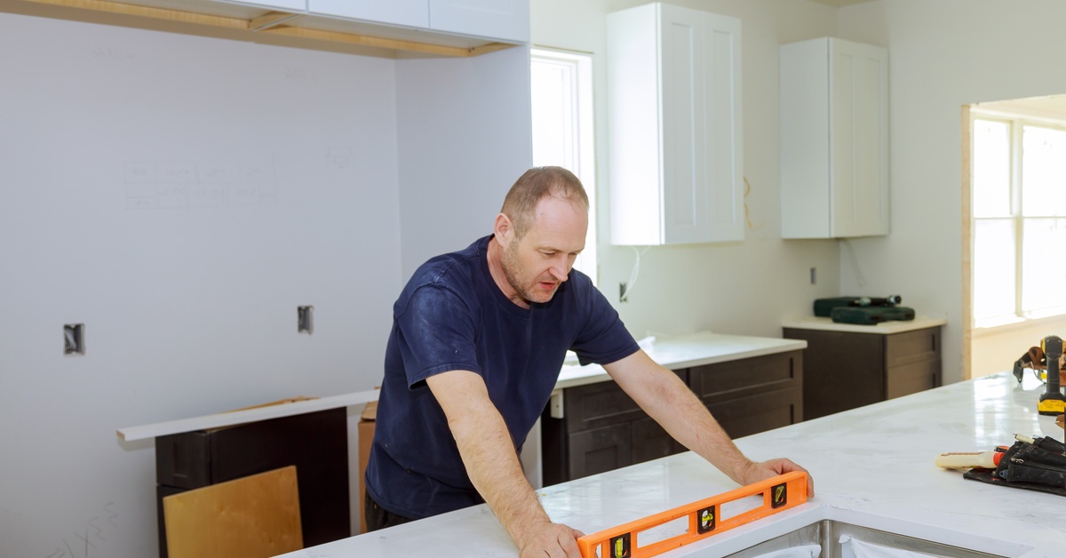A professional installing new countertops holds a leveler on the surface. Various tools are also on the counter.